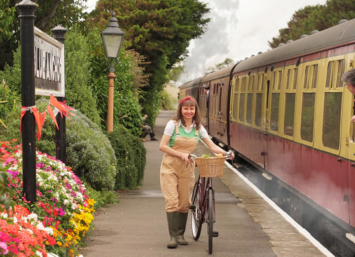 Land Girl walks bike on station platform next to train