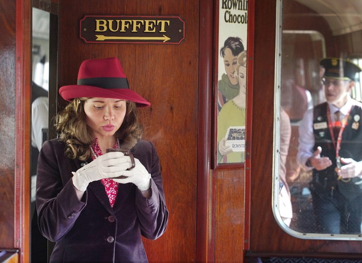 1940s girl blowing on a hot drink in a buffet car of a steam train